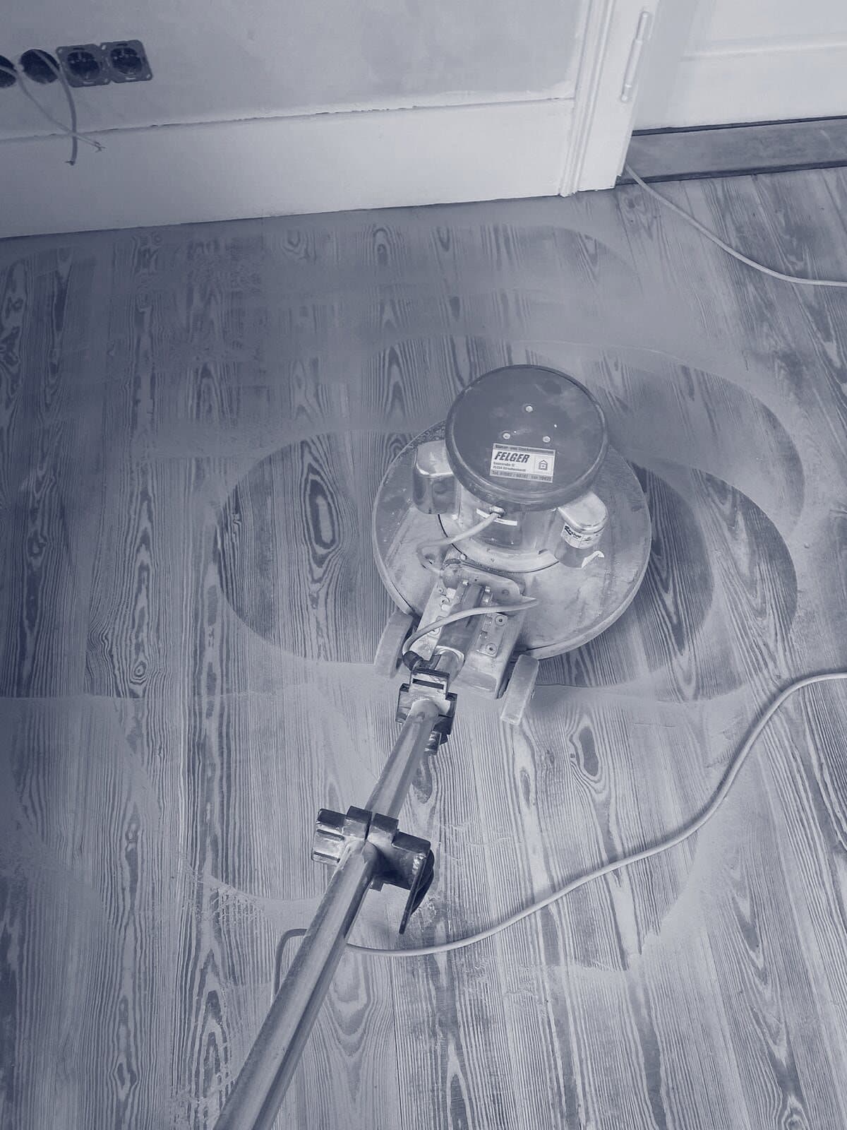 Schleifmaschine auf Holzdielen, um sie herum frisch geschliffene Kreise